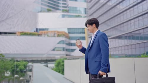 Asian young businessman drinking a cup of coffee while walking in city.