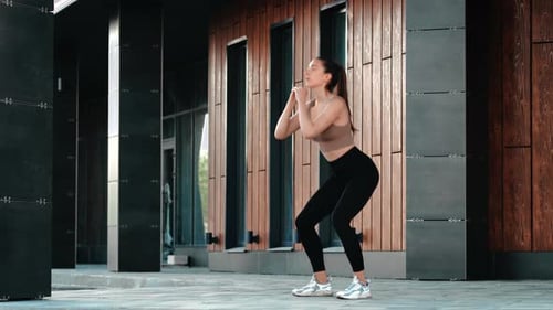 Athletic Young Woman Training Outdoor Doing Squats Buttocks Legs Exercising Modern Building Exterior