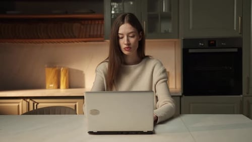Woman Using Laptop in Kitchen Smiles at Camera
