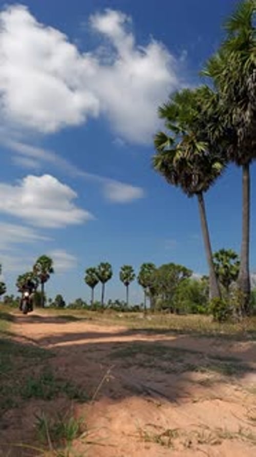 Vertical Low-Angle Motorcycle Ride-By on Dirt Road in Rural Cambodia