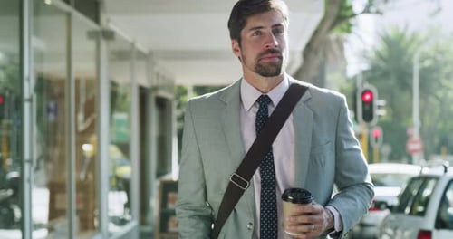4k video footage of a handsome young businessman drinking coffee while walking in the city