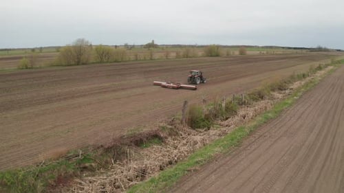 Aerial view from drone following tractor as it plows fertile farm fields to prepare for planting. Co
