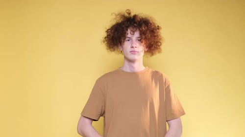Curly Redhaired Man Expressing Displeasure By Gesturing with Hands on Yellow Background in Studio
