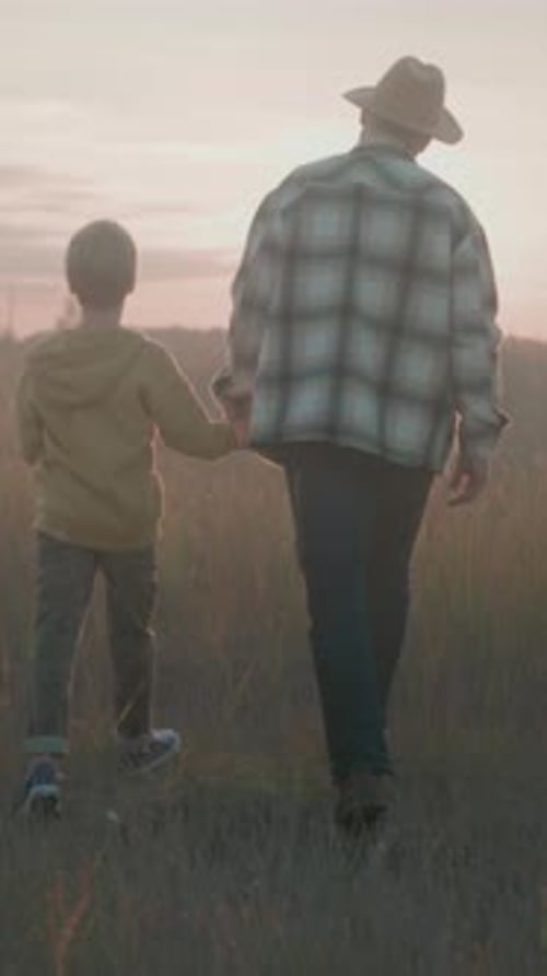 Child and Senior Walk Together in Field at Sunset