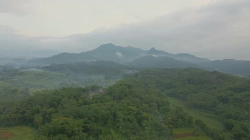 Aerial view of Indonesia rural landscape with view of forest, village and hills in foggy morning.
