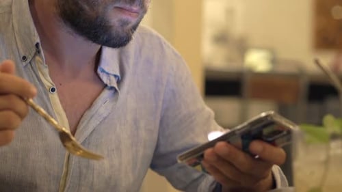 Young man browsing internet on smartphone during evening meal in cafe