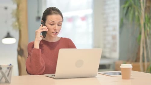 Woman Talking on Phone at Desk with Laptop
