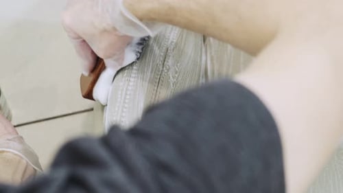 Detailing of the interior of a modern car. A man cleans a beige car seat with a brush and cleaning s