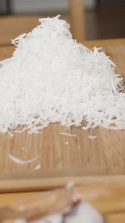 Vertical video. A Pile of Coconut Shavings on a Board and many unprocessed coconuts nearby.