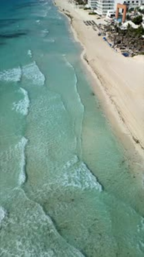Aerial touring a tourist beach. Crystal blue sea. Waves reaching the shore. Sand. Hotels.