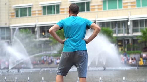 Sporty man stretching body near city fountain in super slow motion preparing for workout