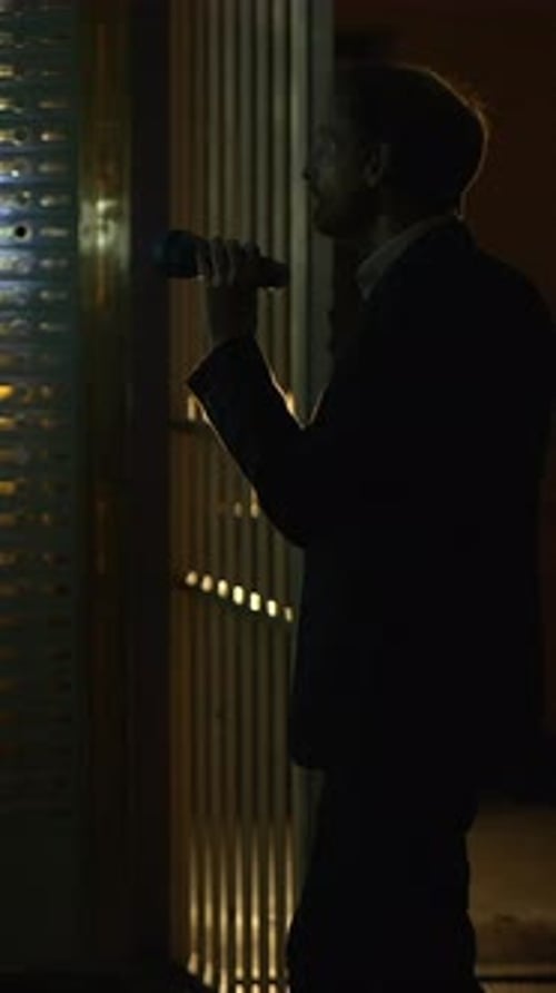 Man Inspecting Wall with Flashlight at Night