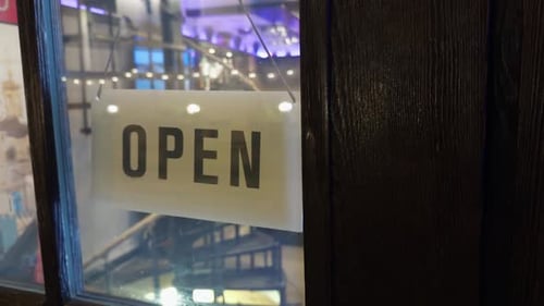 Auf einem Holzschild an der Gebäudefassade steht „Offen“