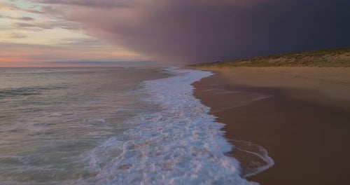 A Drone Flies Over the Ocean's Breaking Wave at Sunset