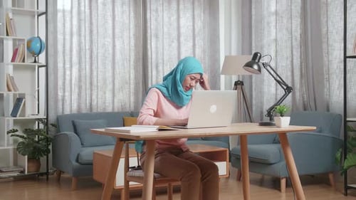 Muslim Woman With A Book On The Table Having A Headache While Working On A Laptop At Home