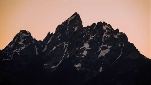 Time Lapse of a big mountain fading away with the sunset leaving the silhouette with an orange backg
