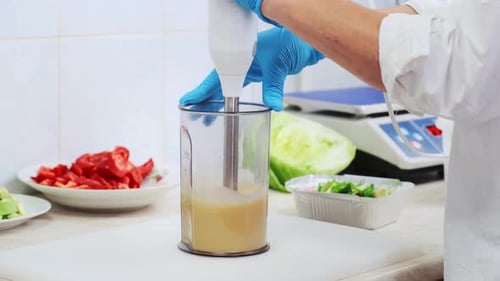 Gloved cook uses immersion blender on kitchen counter