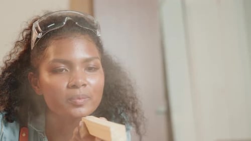 Woman Inspects Wood Piece After Blowing Sawdust Off