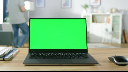 Modern Laptop with Green Mock-up Screen Display Standing on the Desk in the Cozy Living Room. Man w