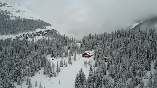 Drone flying towards remote cabin in woods in winter