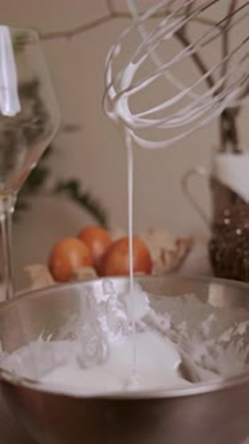 Nahaufnahme, weiße Glasur für Osterkuchen, dicke Glasur, die langsam vom Schneebesen in die Schüssel tropft (Holi).