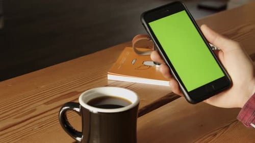 Smartphone with Green Screen Held Over Desk With Coffee