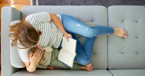 Woman reading book to toddler on couch at home