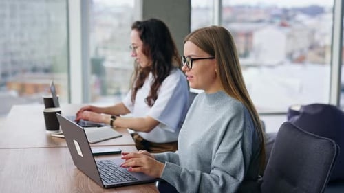 De jeunes collègues féminines positives travaillent sur des ordinateurs portables au bureau. Ambiance de travail calme.
