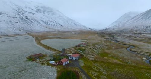 flying over farm in frozen valley with river and mountains on background