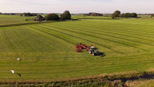 drone footage of a farmer on a tractor with hay rake working on a green agricultural field in the