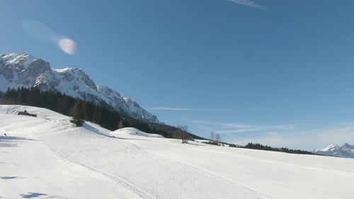 Panoramic shot taken from a ski lift moving uphill with skiers, in the background a panorama of snow
