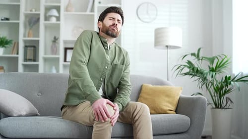 Adult Male Sitting on Sofa with Knee Pain