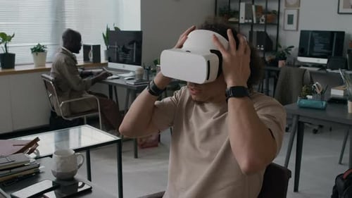 Young Web Engineer Putting on VR Headset while Working on Laptop in Office