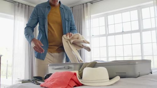 Young Adult Packing Suitcase for Travel in Bedroom