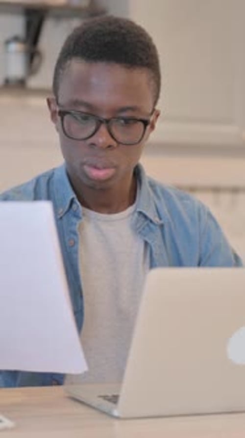 Young Man Reviews Documents At Laptop Indoors