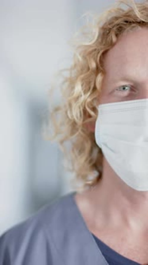 Vertical video of portrait of caucasian male doctor with blonde hair, wearing face mask, slow motion