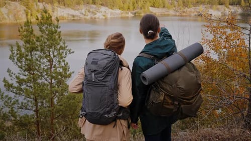 Couple with Backpacks Admiring Lake Among Autumn Forest