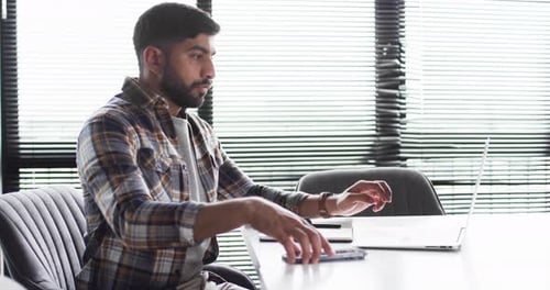 Young Asian businessman in a plaid shirt uses a smartphone in an office setting for business purpose