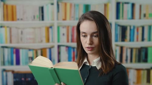 A Young Woman Enjoying Reading a Book in a Quiet Library Environment with Bookshelves