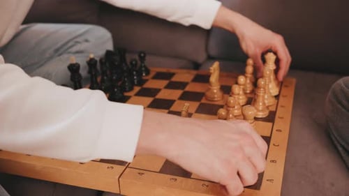 Close Up Hands of Dad and a Daughter are Playing Chess on a Wooden Board on a Couch in a Room They
