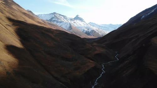 Sonnenbeschienene Schlucht mit fließendem Fluss, Filmmusik Drohnenaufnahmen von rauschenden Bächen und schneebedeckten Gipfeln