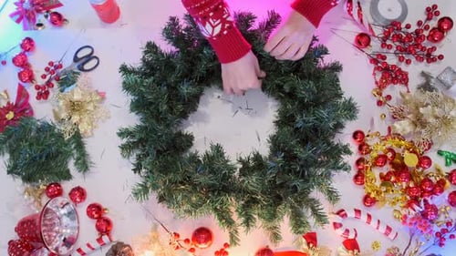 Hands Crafting Christmas Wreath with Holiday Decorations