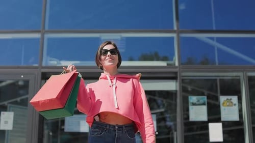 Casual Female in Sunglasses Leaving Mall with Paper Bags
