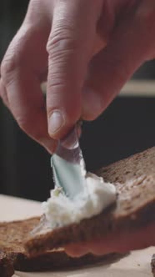 Close-up of Unrecognizable Hands Spreading Cream Cheese Onto Bread with Knife