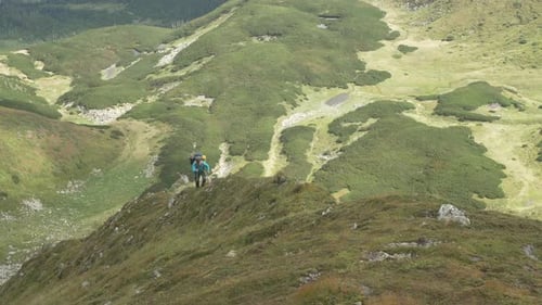 A Tourist with Sticks Climbs to the Top of the Mountain Along the Ridge