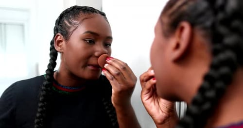 Woman Applying Makeup with Sponge in Front of Mirror
