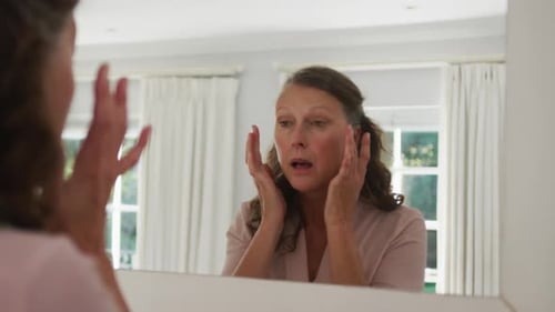 Woman Applies Cream to Face in Bathroom Mirror