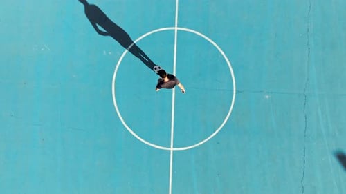 Soccer Player Plays Ball Trick in Blue Field Overhead View