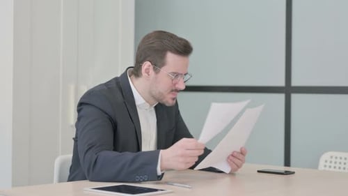 Frustrated Businessman Reviewing Documents at Desk in Office