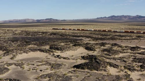 Extremely long freight train speeds quickly down a completely straight train track through a desert